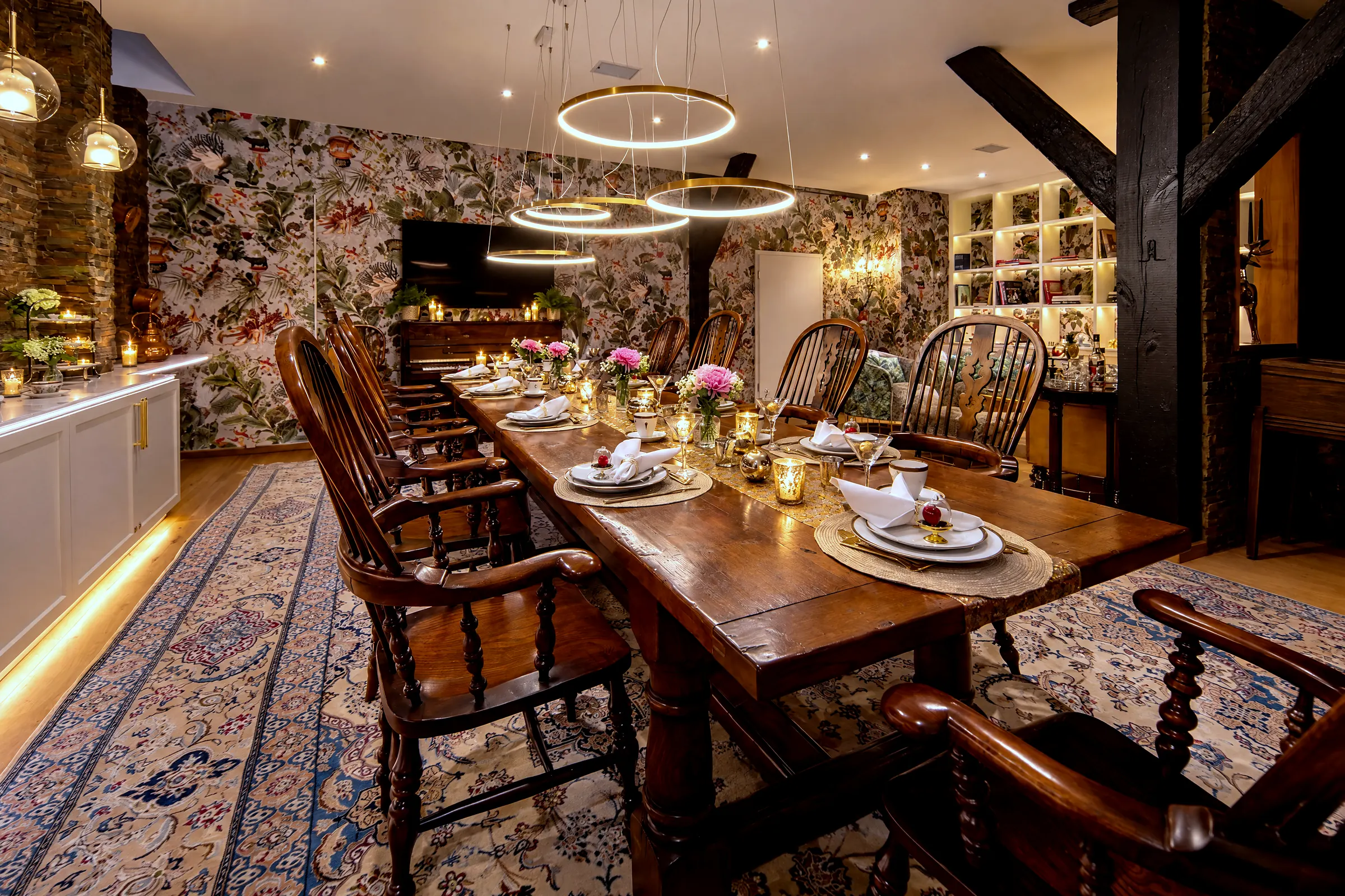 De lange tafel 's avonds, gedekt voor het diner, met de bibliotheek en de lounge met open haard erachter en links de piano